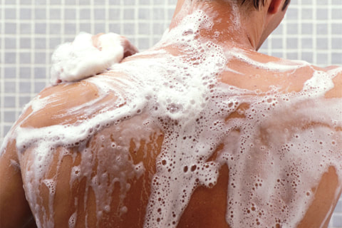 Photo of a man easily soaping up his back in the shower due to soft water.